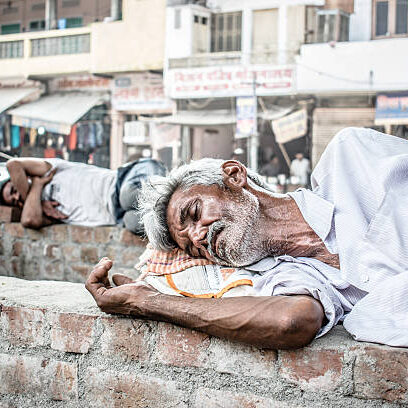 An old homeless man taking a nap on a brick wall that is built along the road on a very hot summer afternoon.